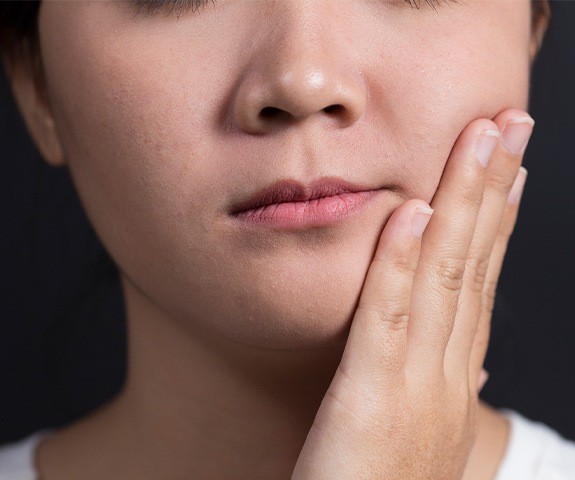 Young woman in need of pulp therapy holding cheek