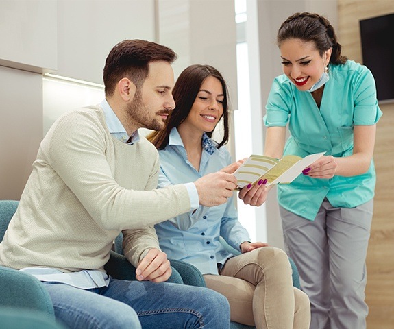 Dental team member and patients reviewing dental insurance forms